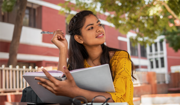 a student outside of a school holding a notebook and pen