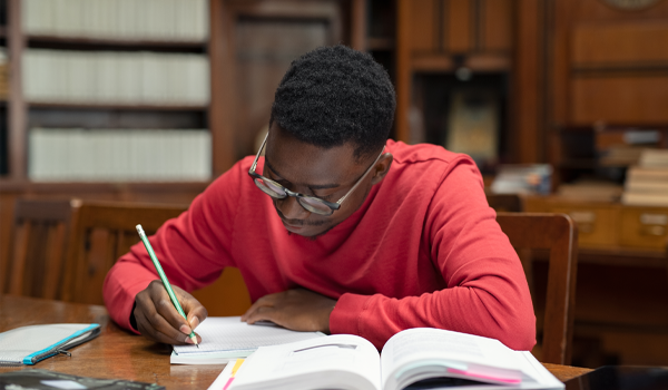 A student wearing glasses and a sweater studies carefully in a library.