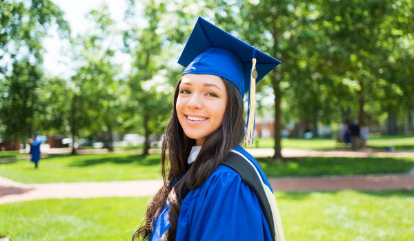 female student in blue cap and gown smiling outdoors