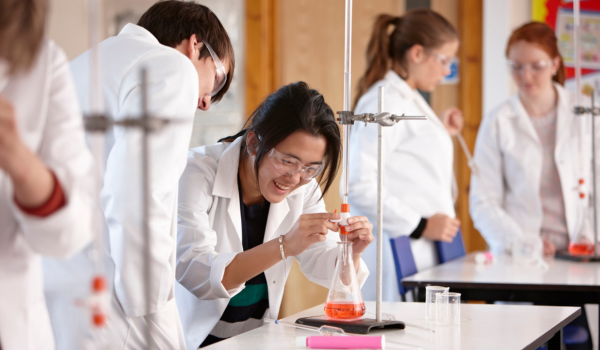 students in lab coats gather around a beaker of liquid