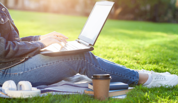 a sunlit laptop sitting in a lap on a green lawn