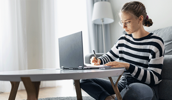 a student sits at a coffee table with a laptop and notebook