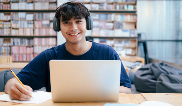 a smiling student with headphones in front of an open laptop