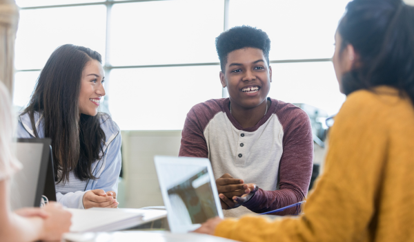 3 students having a conversation over notes and a laptop