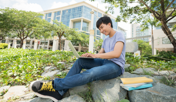 student sitting outside a college building on his laptop